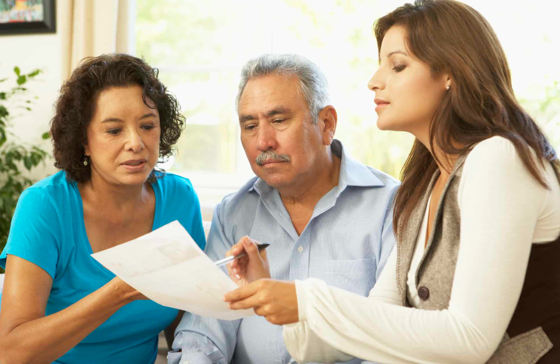 Asesora explicando documentos de planificación a una pareja adulta como parte de la protección y el legado familiar.